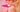 The rear of a person wearing pink lingerie, holding a Fun Factory vibrator behind their back with kiss marks on their butt cheeks